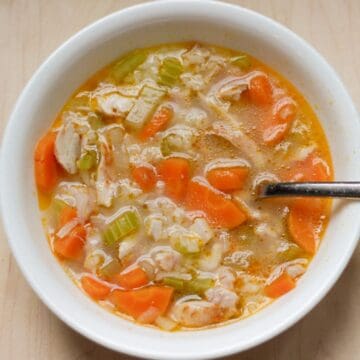 Chicken and rice soup made with roasted chicken, carrots, and celery is served in a white bowl.