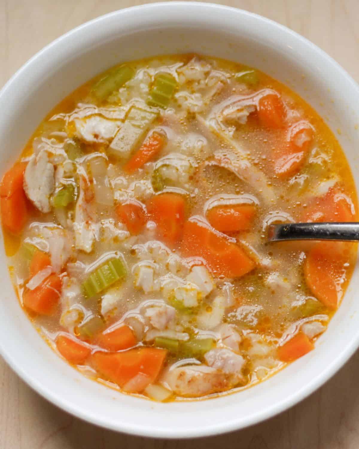 Chicken and rice soup made with roasted chicken, carrots, and celery is served in a white bowl.