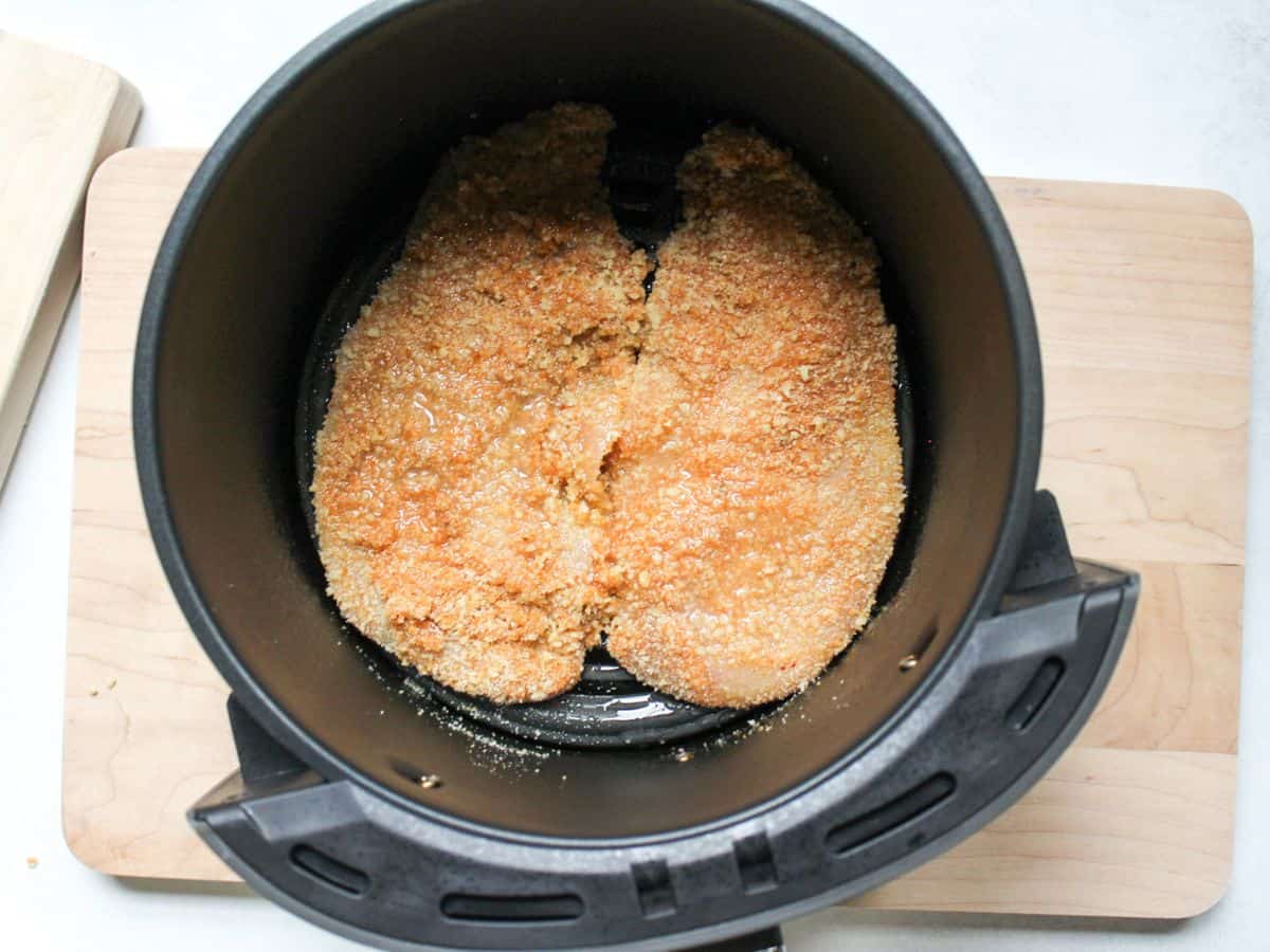 Two breaded chicken schnitzels coated lightly in oil arranged in air fryer basket.