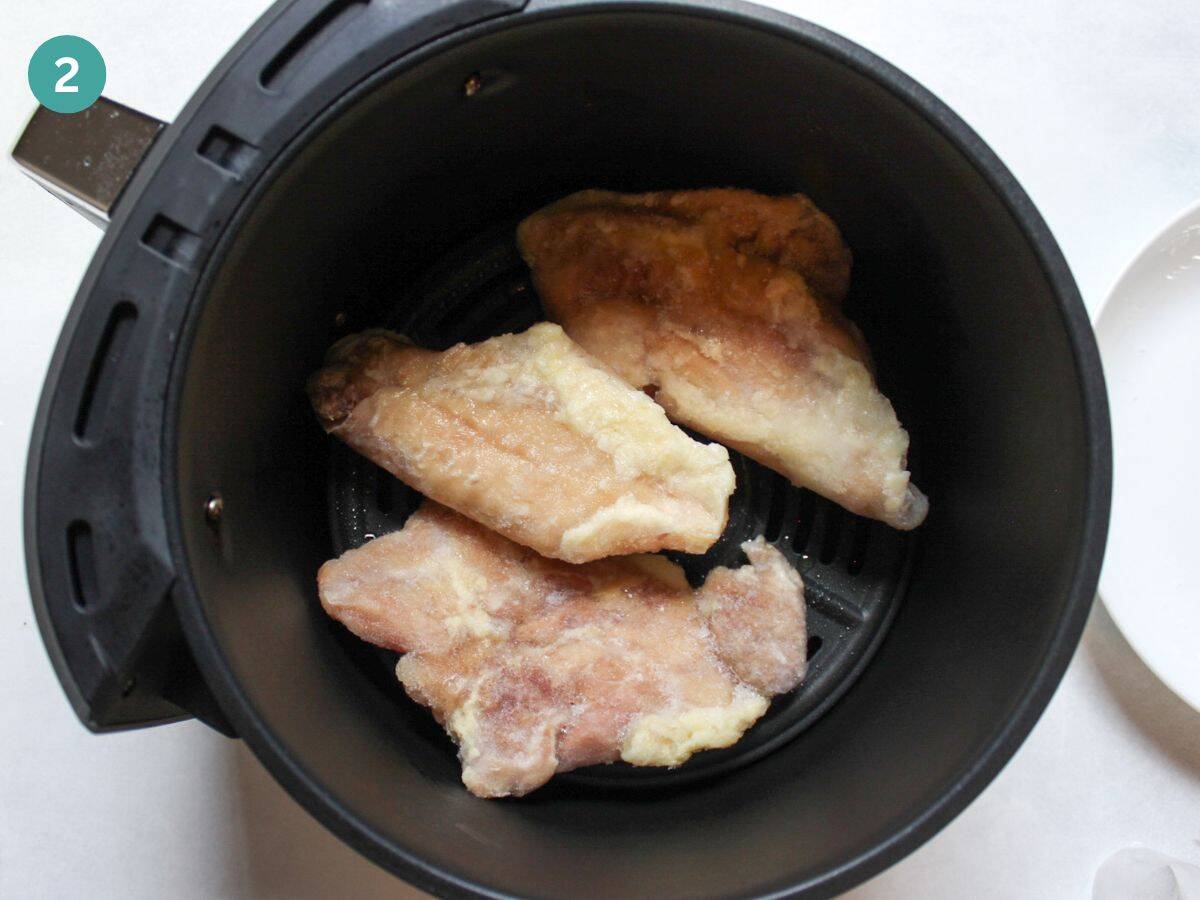 Frozen chicken thighs placed in air fryer basket.