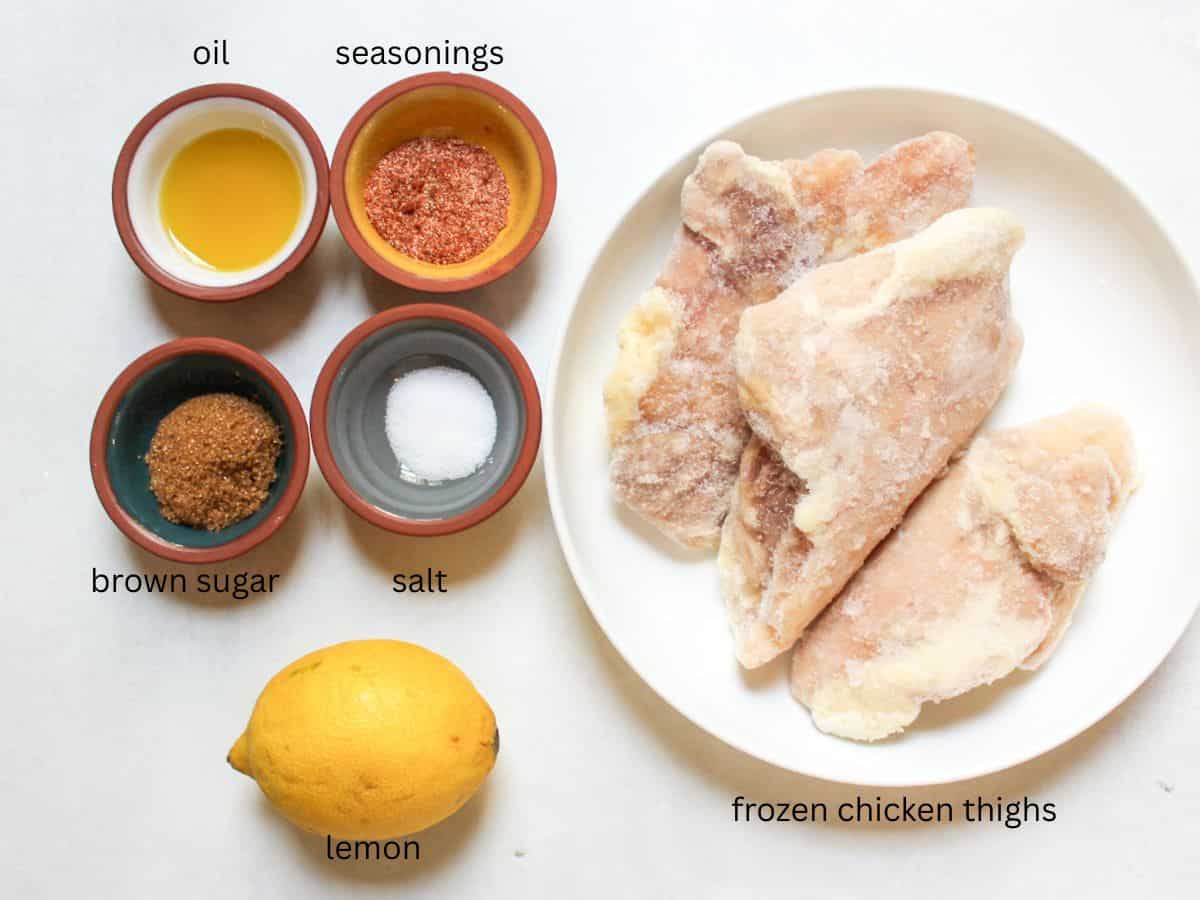 Recipe ingredients on a white background: frozen boneless chicken thighs, oil, seasonings, salt and a lemon.