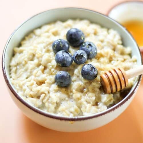 Creamy honey oatmeal served in a bowl, topped with fresh blueberries and drizzled with honey using a wooden honey dipper.