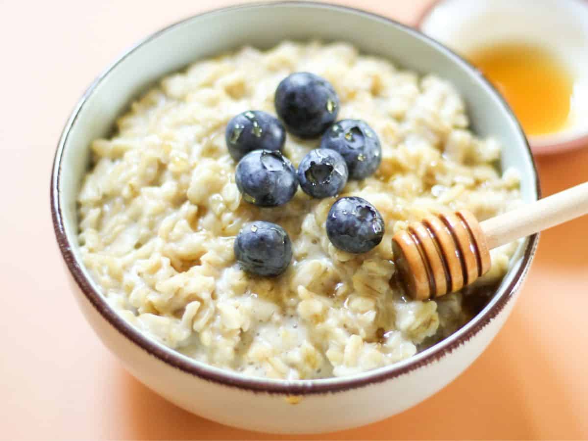 Bowl of creamy honey oatmeal topped with blueberries and a drizzle of honey using a wooden dipper.