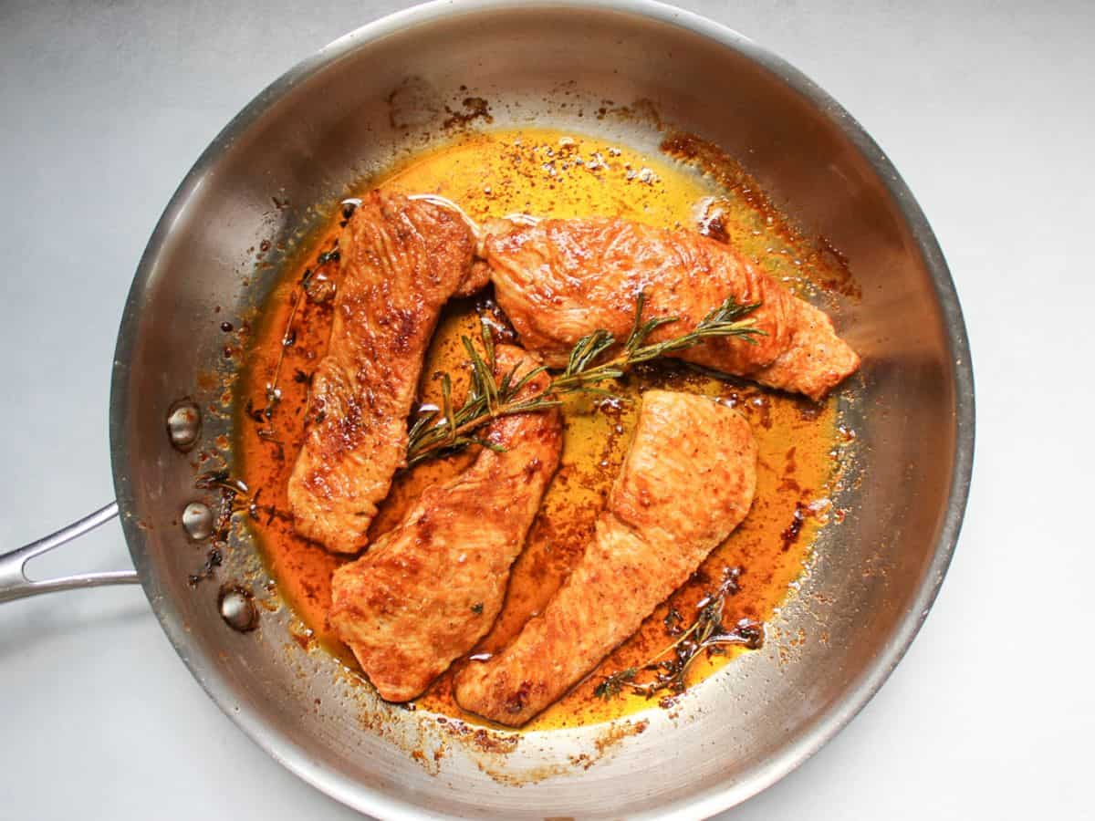 Pan-fried turkey steaks in a frying pan.