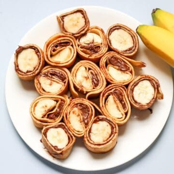 Crepe roll-ups with Nutella and bananas on a white plate.
