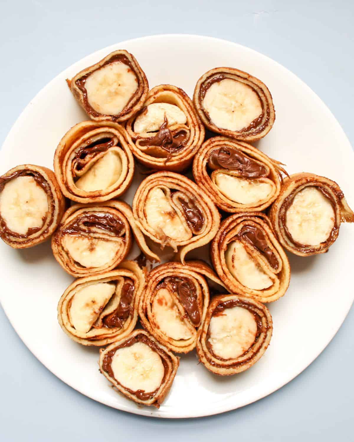 Rolled banana and Nutella crepes sliced into bite-sized pieces on a plate.