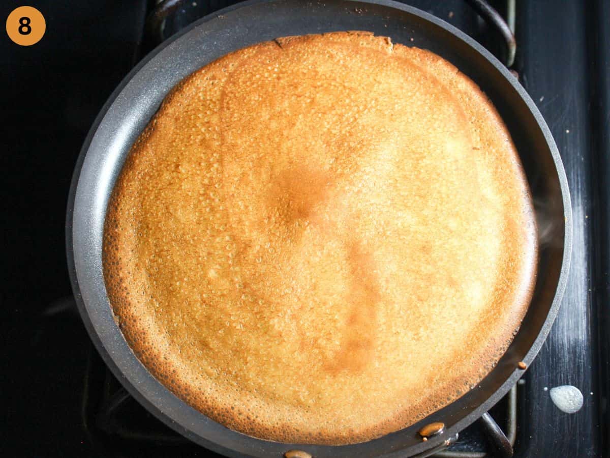 Golden-brown crepe flipped in a crepe pan, cooking on the second side.