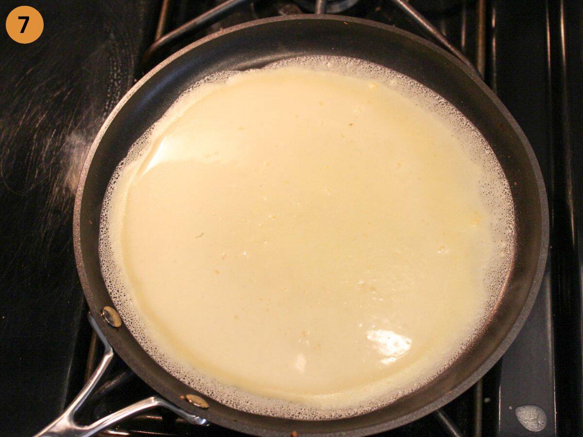Thin crepe cooking on one side in a hot pan, uncooked on top.