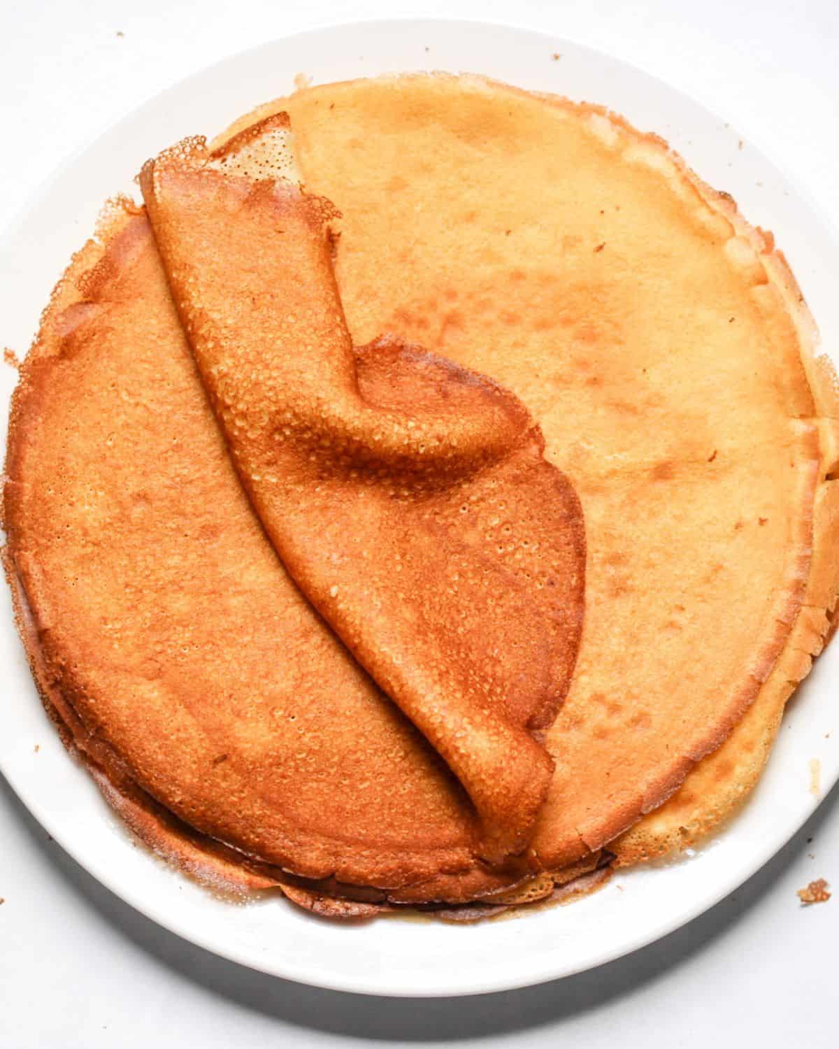 Thin French crepes stacked on a plate, top crepe folded to highlight texture.