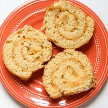 Slices of soft apple cake roll with apple filling in the center, beautifully served on orange plate.