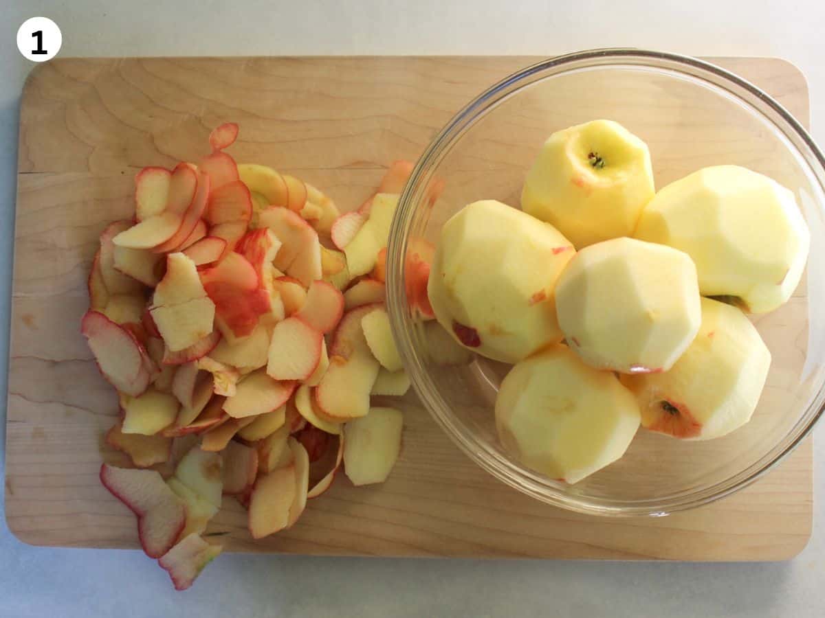 Peeled apples in a glass bowl with the peels right next to it. 