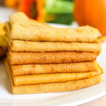 Folded pumpkin crepes stacked on a white plate, ready to serve.