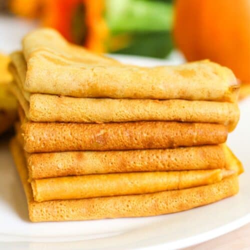 Folded pumpkin crepes stacked on a white plate, ready to serve.