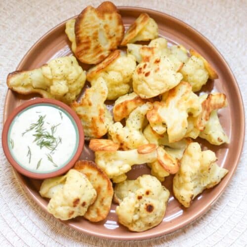 Baked ranch cauliflower florets served on a brown plate with a side of creamy dipping sauce.
