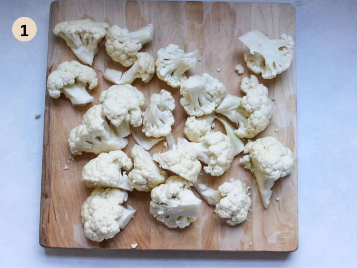 Cauliflower cut in to florets on a cutting board.