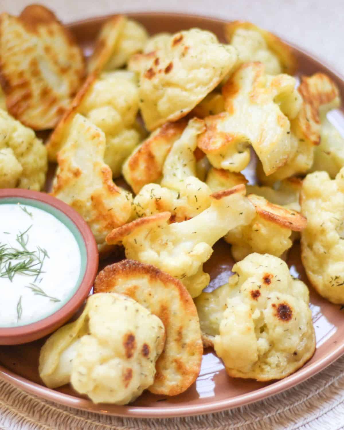 Golden battered cauliflower florets served with a side of ranch sauce.