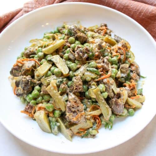 Creamy chicken liver salad with onion, carrots, peas and pickled served in a white bowl.
