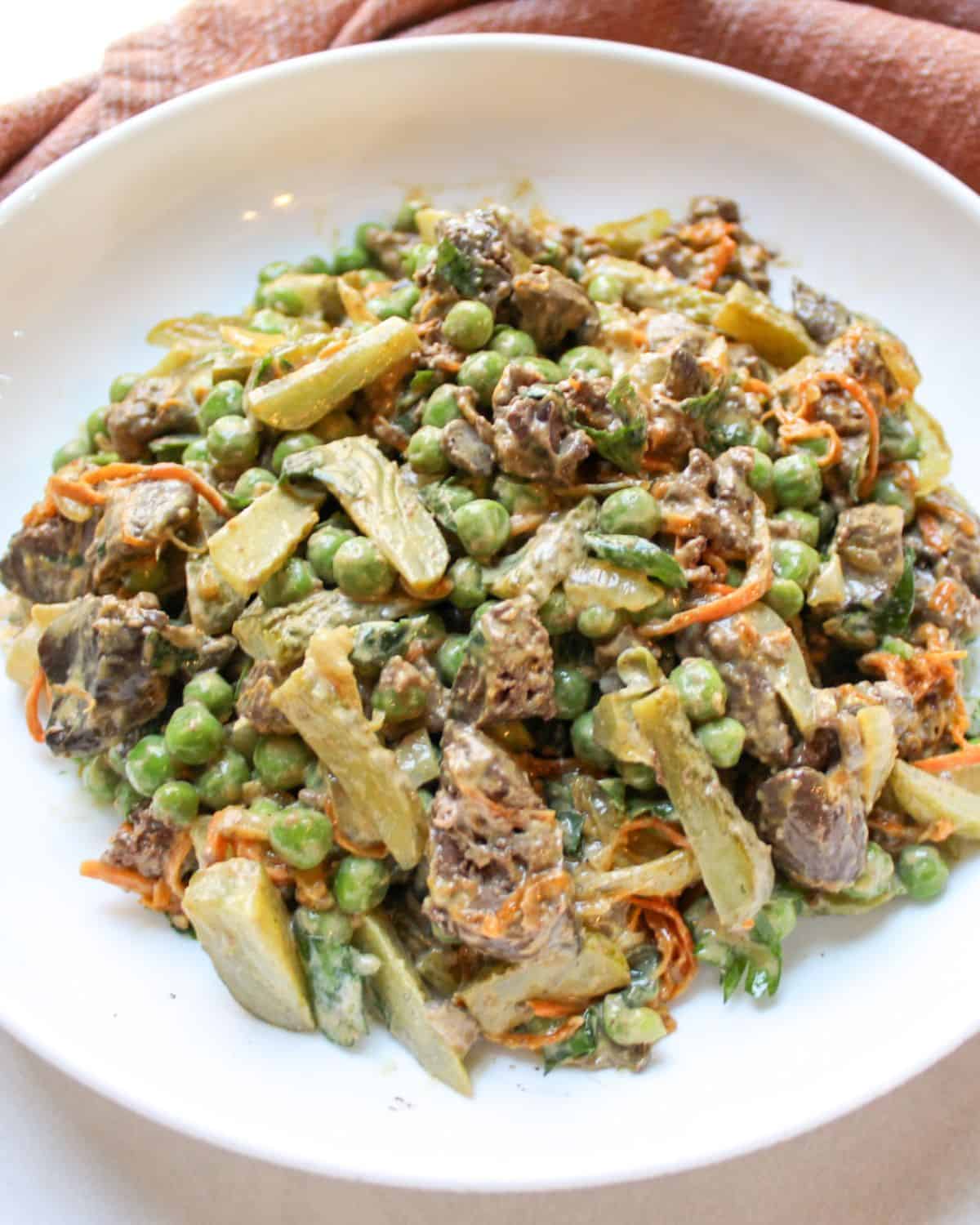Creamy chicken liver salad with onion, carrots, peas and pickled served in a white bowl.