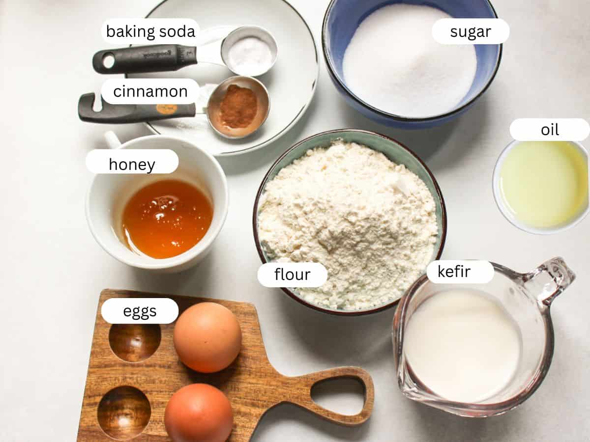 Ingredients for honey cake laid out on a table: flour, honey, sugar, eggs, kefir, oil, eggs, baking soda and cinnamon.