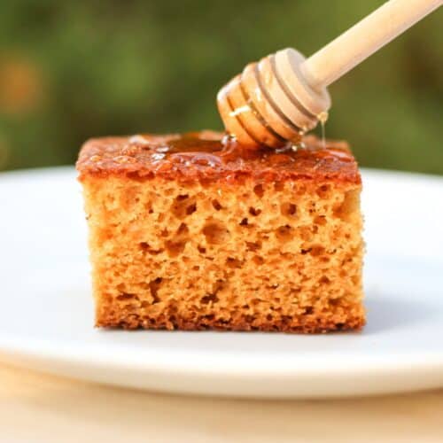 Homemade honey cake slice with a drizzle of honey from a wooden honey dipper.