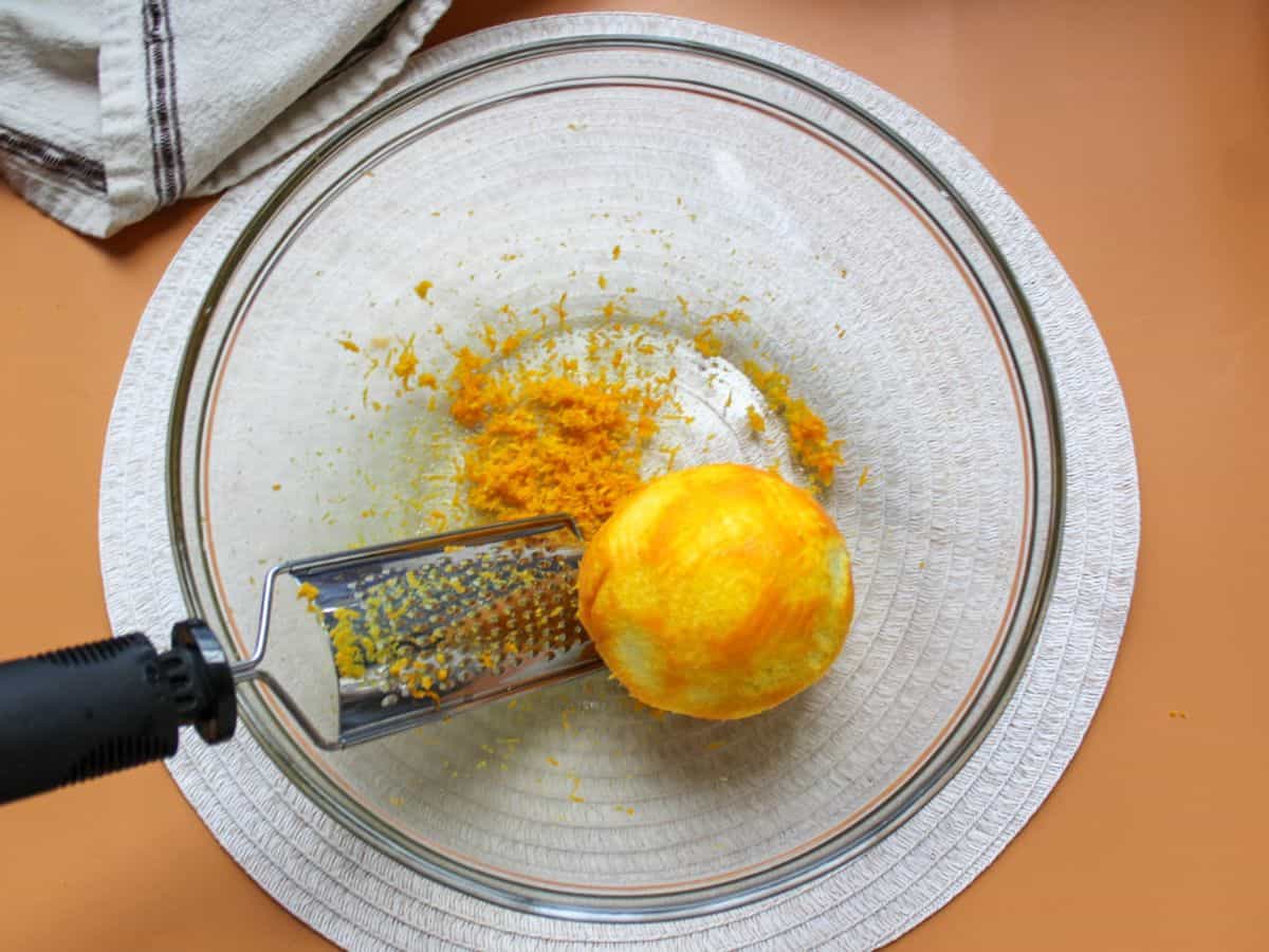 Zesting a naval orange into a large bowl using a fine zester.