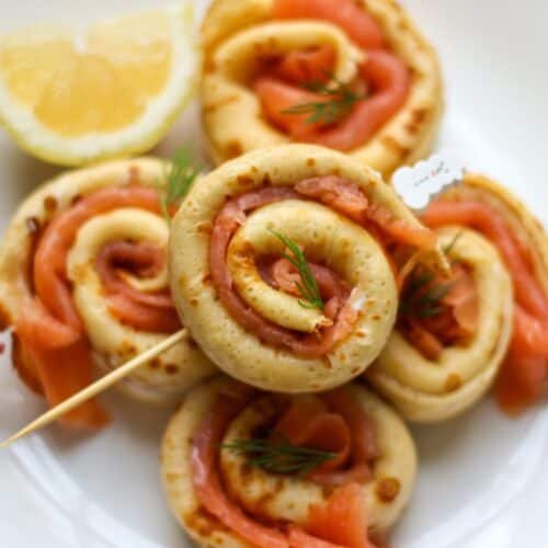 Smoked salmon crepe roll-ups arranged on a serving plate as elegant appetizer.