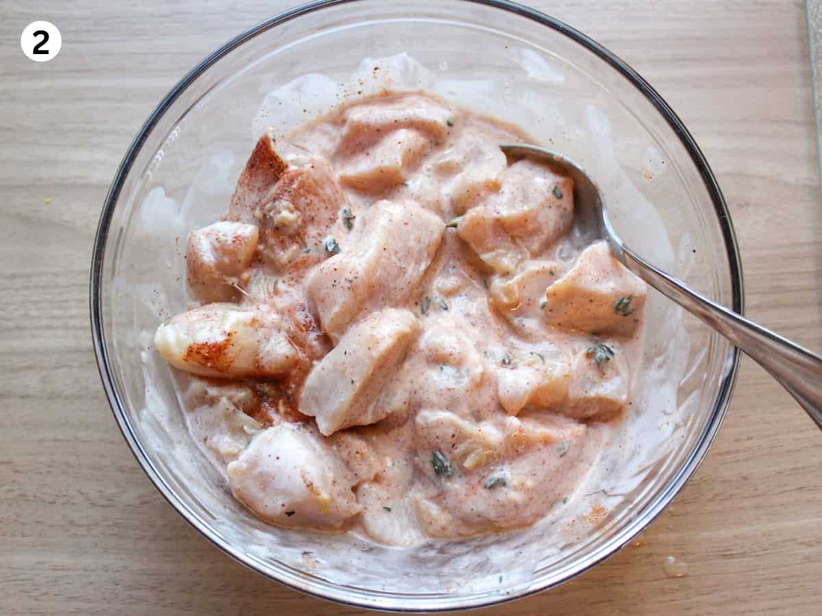 Chicken pieces are marinating in a creamy garlic marinade in a glass bowl. 