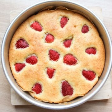 Easy one-bowl strawberry cake baked in a round baking pan with strawberries on top.