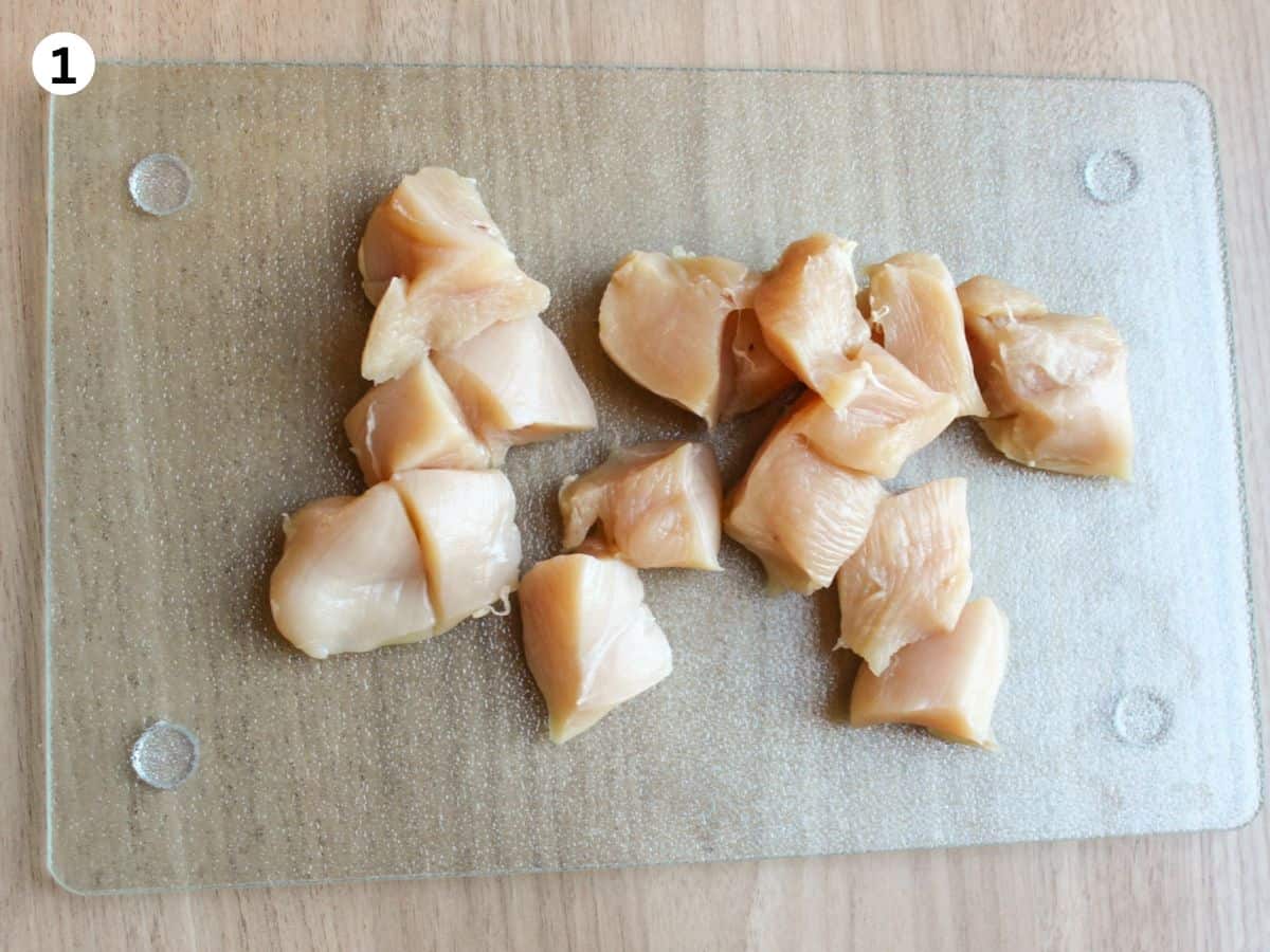 Cubed raw chicken breast on a glass cutting board for chicken skewers. 