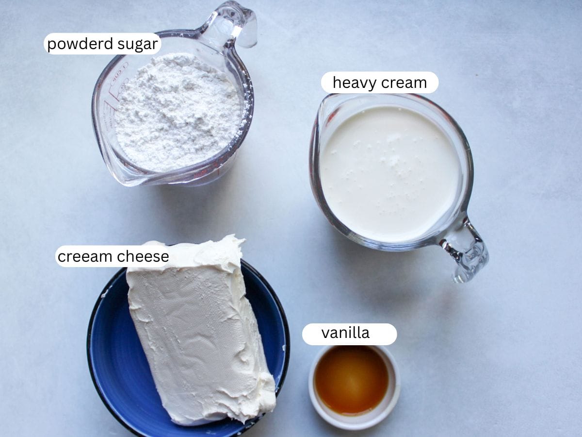 Cream cheese frosting ingredients on a table, including cream cheese, heavy whipping cream, powdered sugar and vanilla extract. 