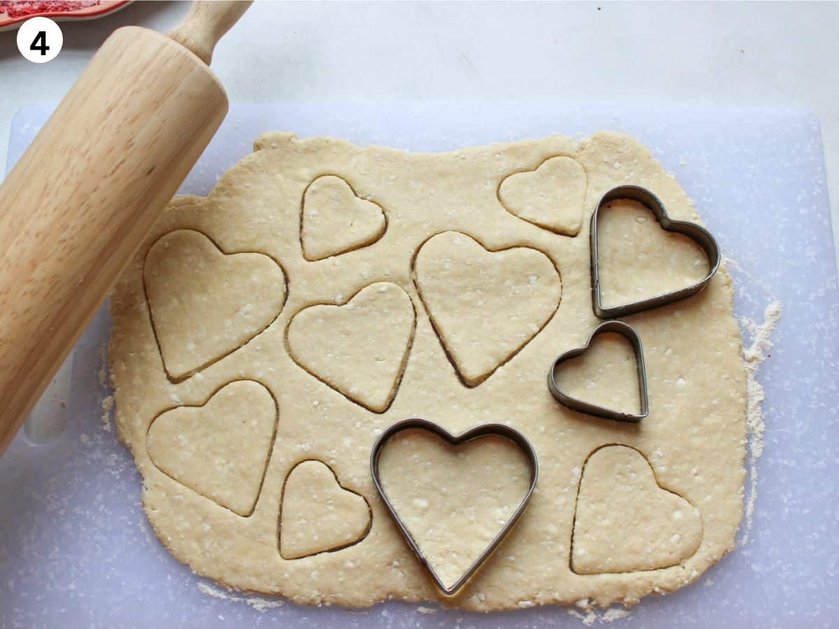 Rolling out cookie dough and cutting heart shaped cookies with a cookie cutter.