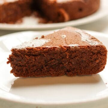 A slice of flourless Italian chocolate almond cake served on a white plate dusted with powdered sugar.