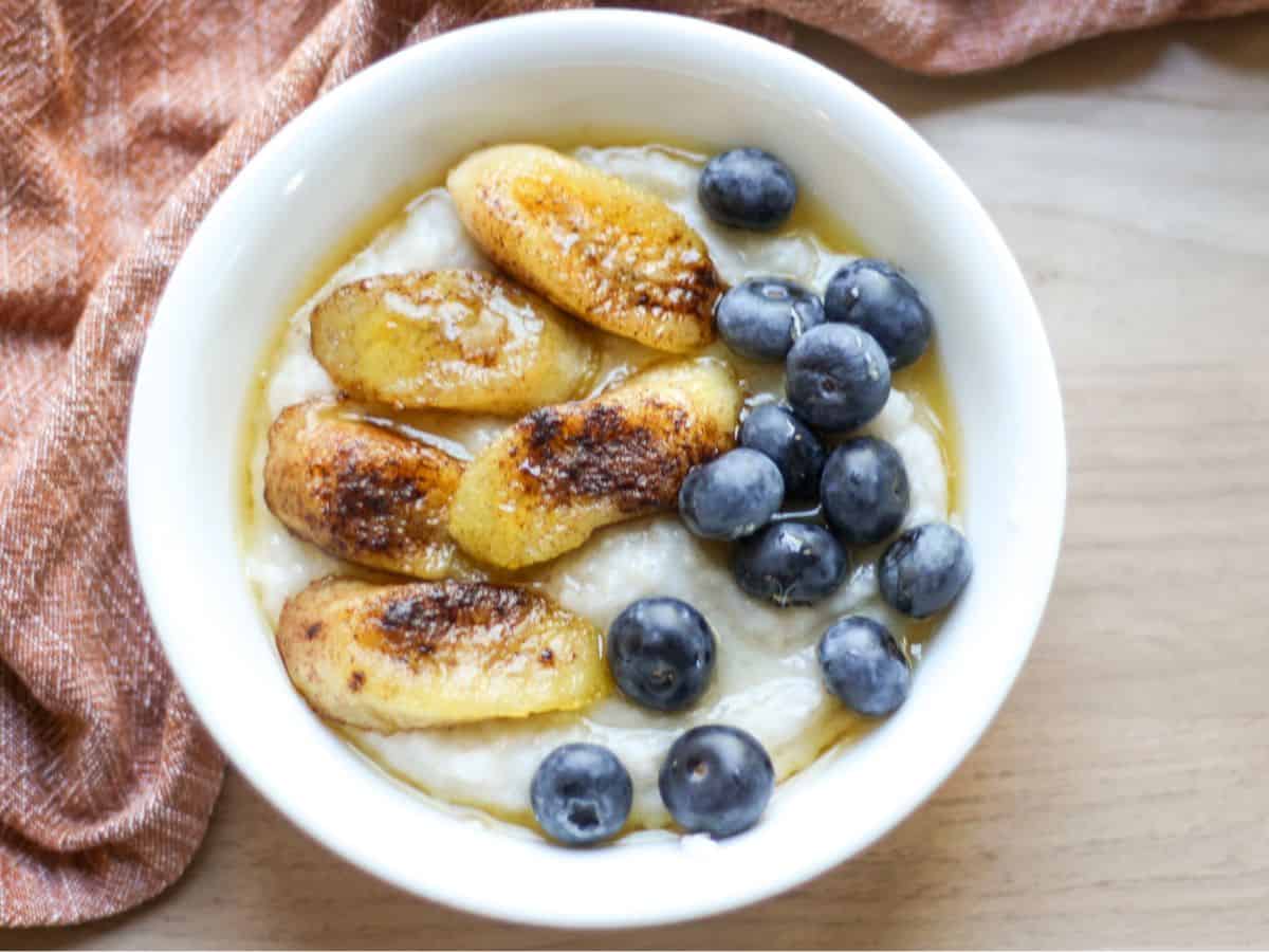 Serving the cream of buckwheat porridge in a bowl, topped with caramelized banana slices, fresh blueberries, and a drizzle of honey.