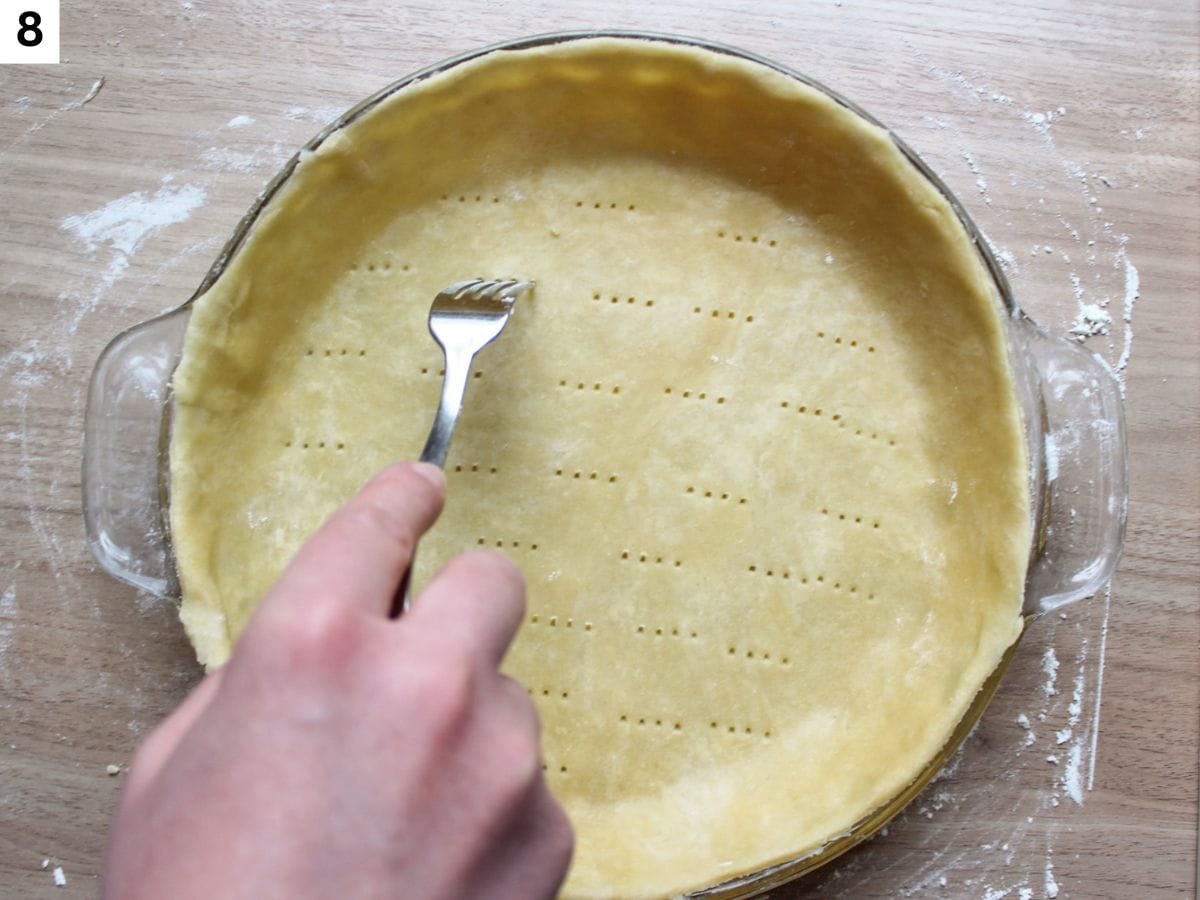 Piercing the surface of the tart crust with a fork to prevent it from puffing. 