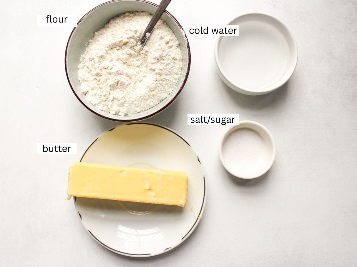 French tart crust 4 ingredients on a white surface, including flour, salt/sugar, cold butter and cold water. 