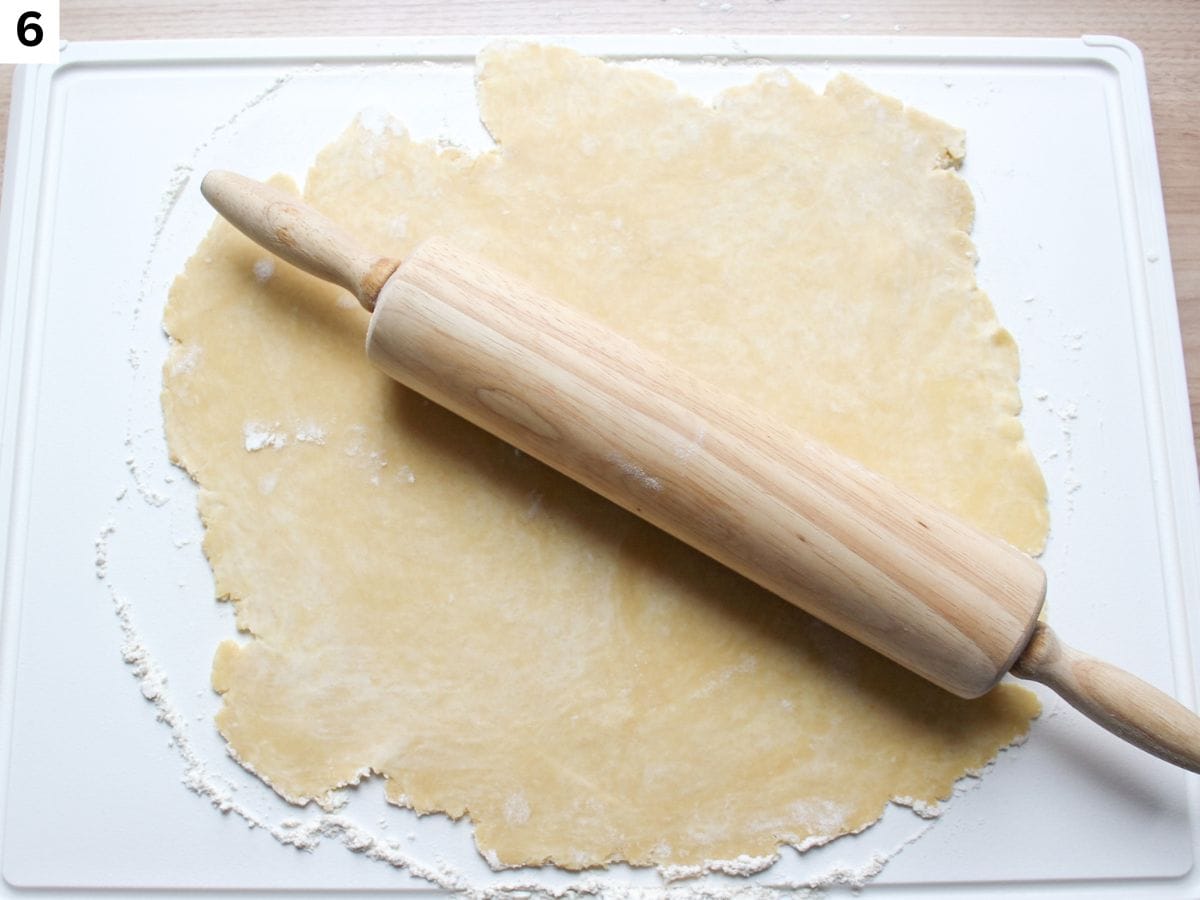 Rolled out dough into a thin circle using a wooden rolling pin.
