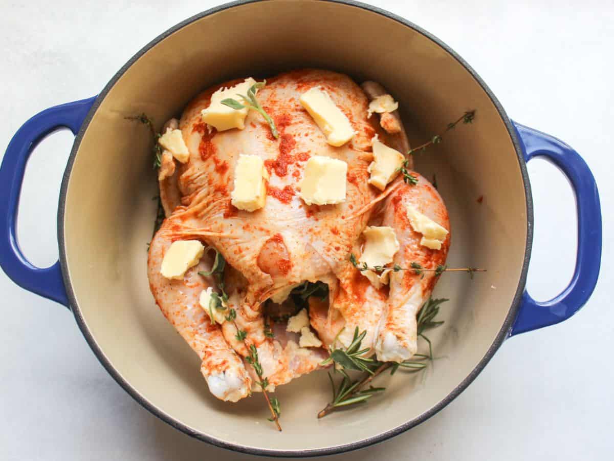Seasoned chicken placed in a dutch oven, cubes of butter added on top of chicken.