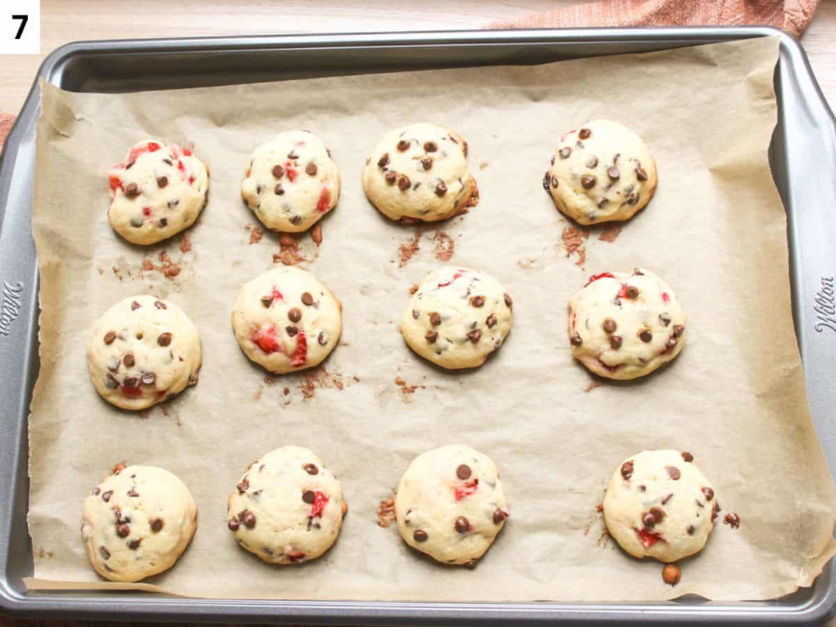 Baked soft chocolate chip cookies with strawberry pieces on baking pan.