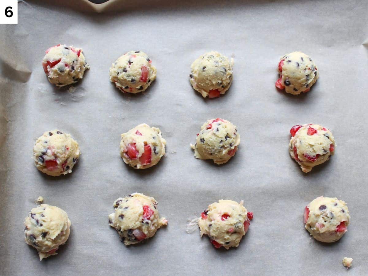 Strawberry chocolate chip cookie dough balls arranged on a baking pan lined with parchment paper.