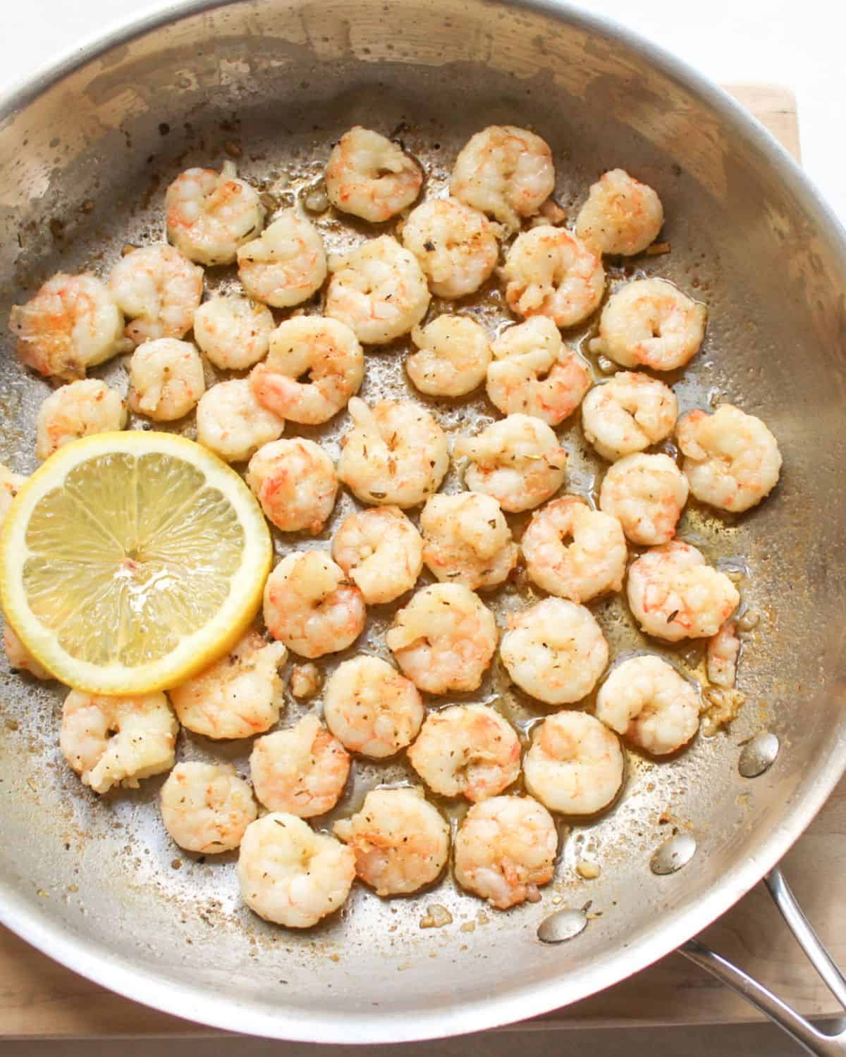 Juicy pan-fried shrimp in  a stainless steel skillet with a slice of lemon.