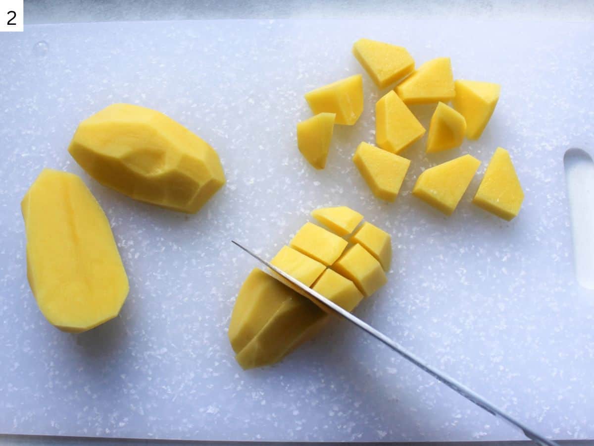 Cutting the potato into 2 inch chunks on a plastic cutting board. 