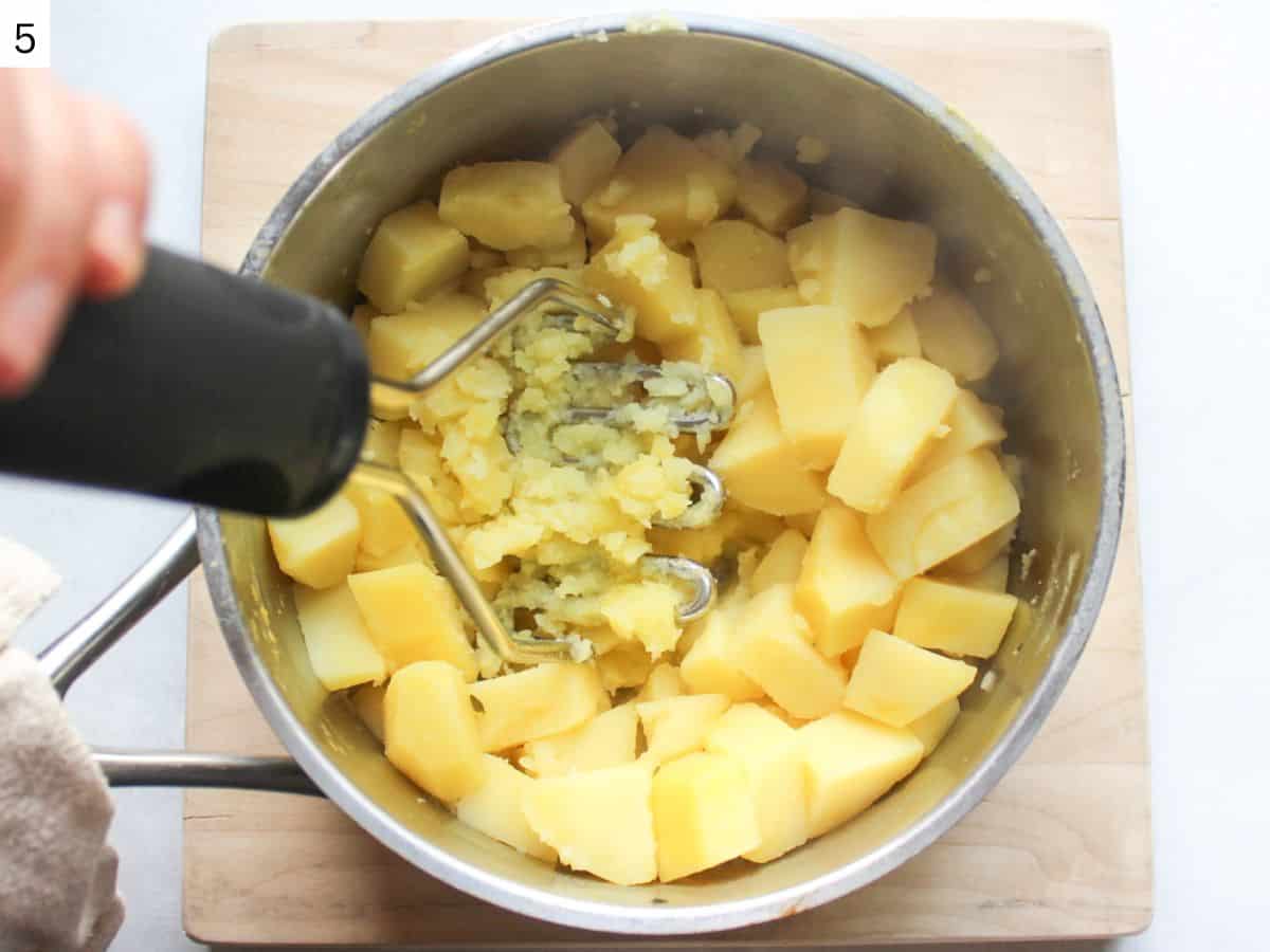 Mashing cooked potatoes with a wire potato masher in a pot. 