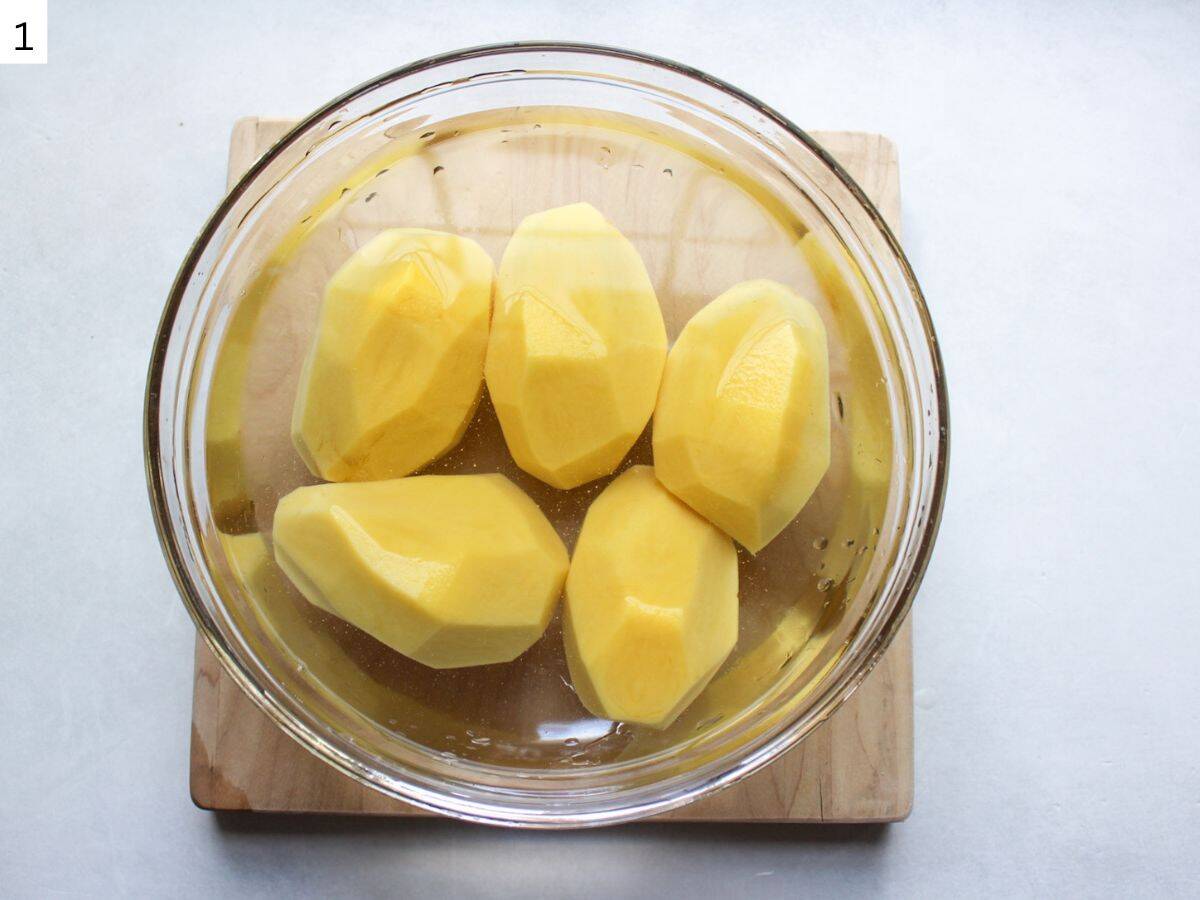 Peeled potatoes in a bowl filled with cold water. 