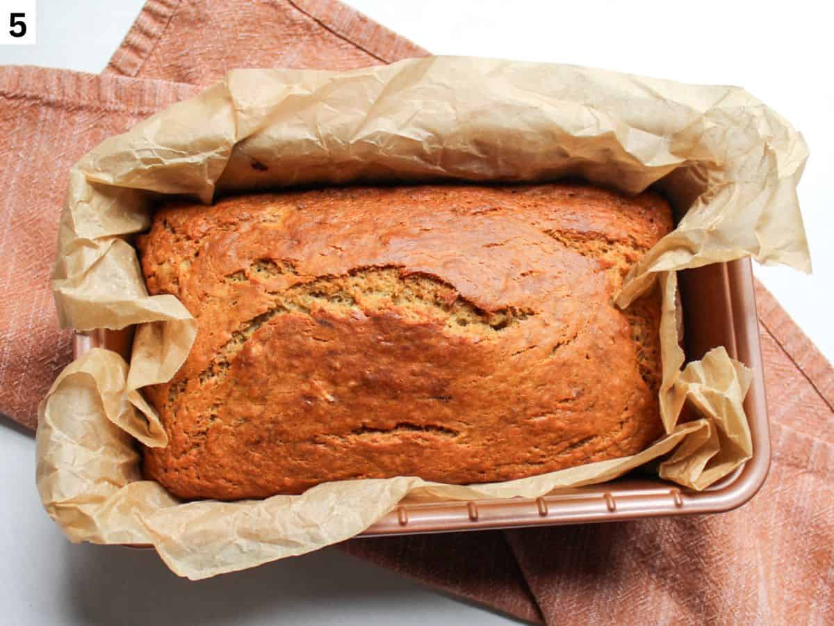 Freshly baked honey  banana bread with a cracked top in a loaf pan. 