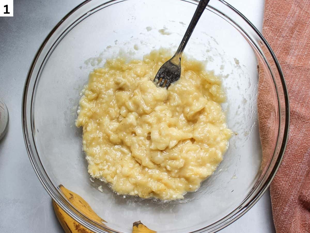 Over-ripe mashed bananas in a large glass bowl with a fork. 