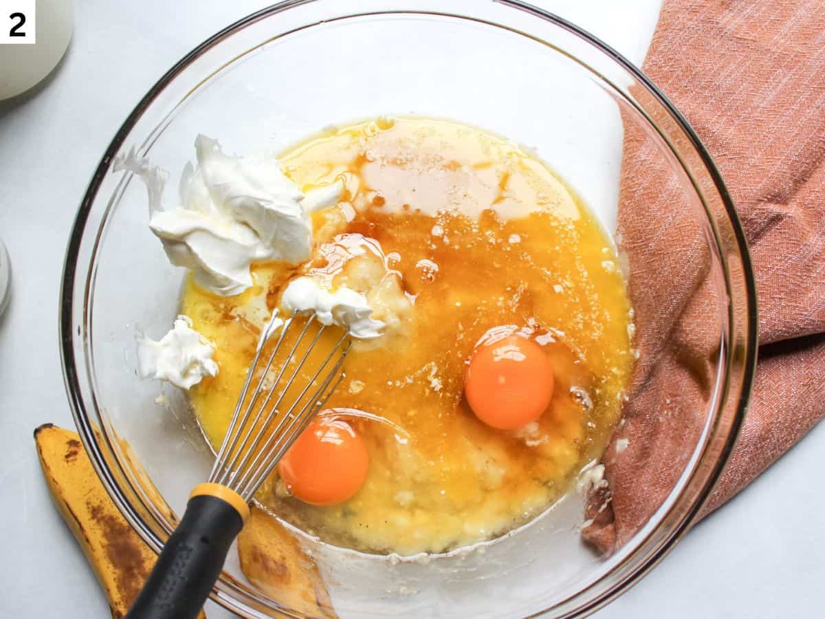 Eggs, honey, sour cream, melted butter added to the bowl with mashed bananas. 