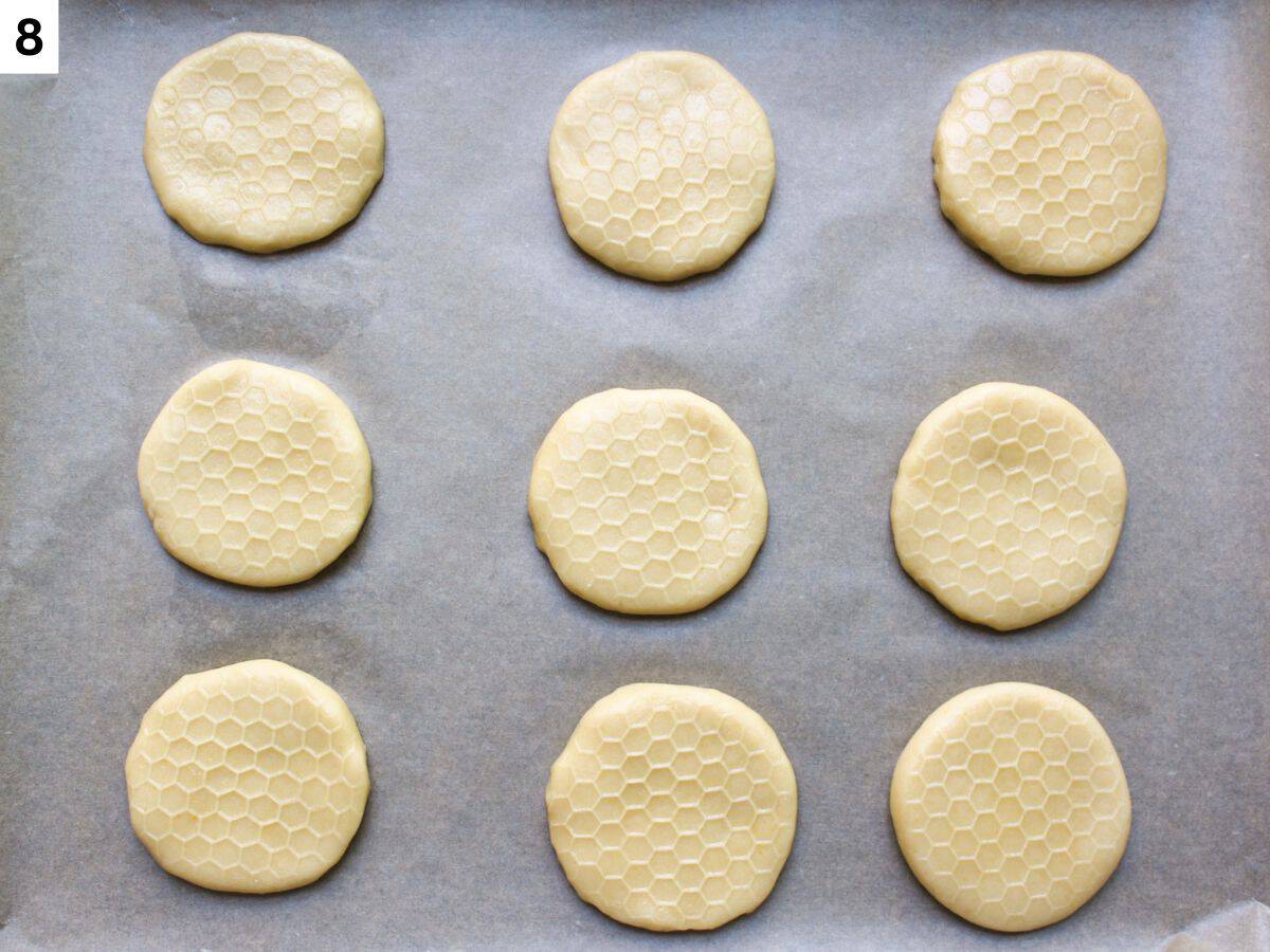 Honey cookies with honeycomb prints on top arranged on a baking pan lined with parchment paper. 