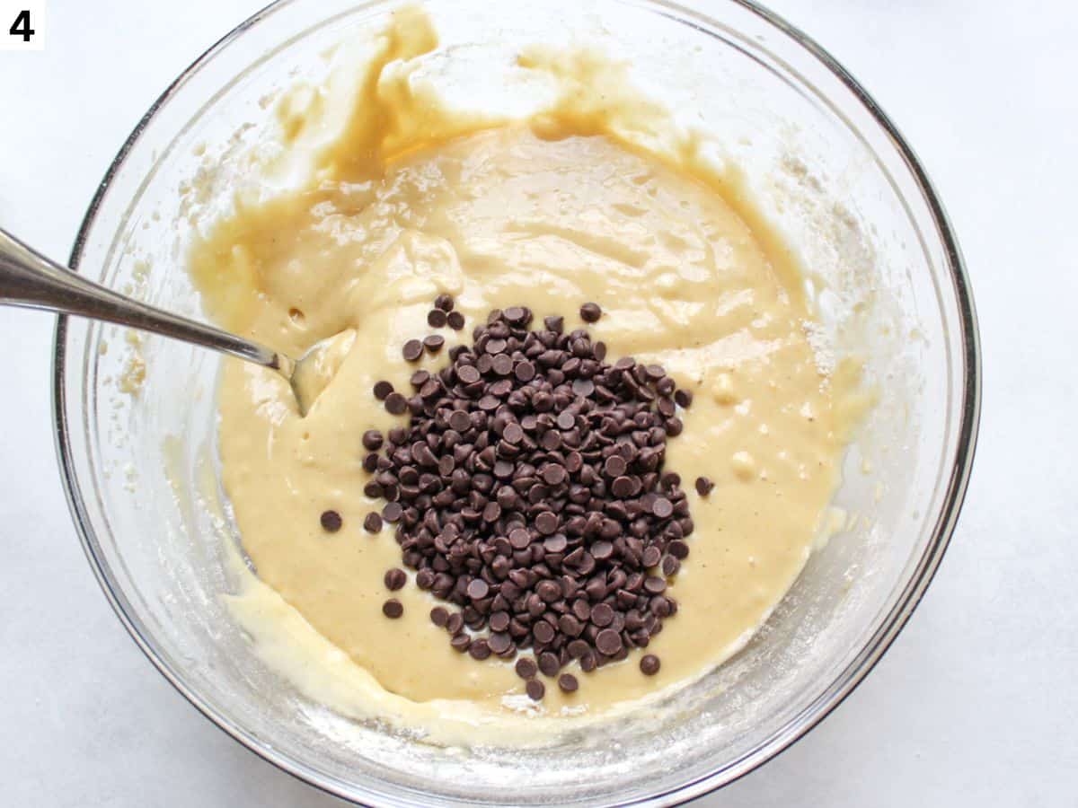 Chocolate chips added to the muffin batter in a glass bowl. 