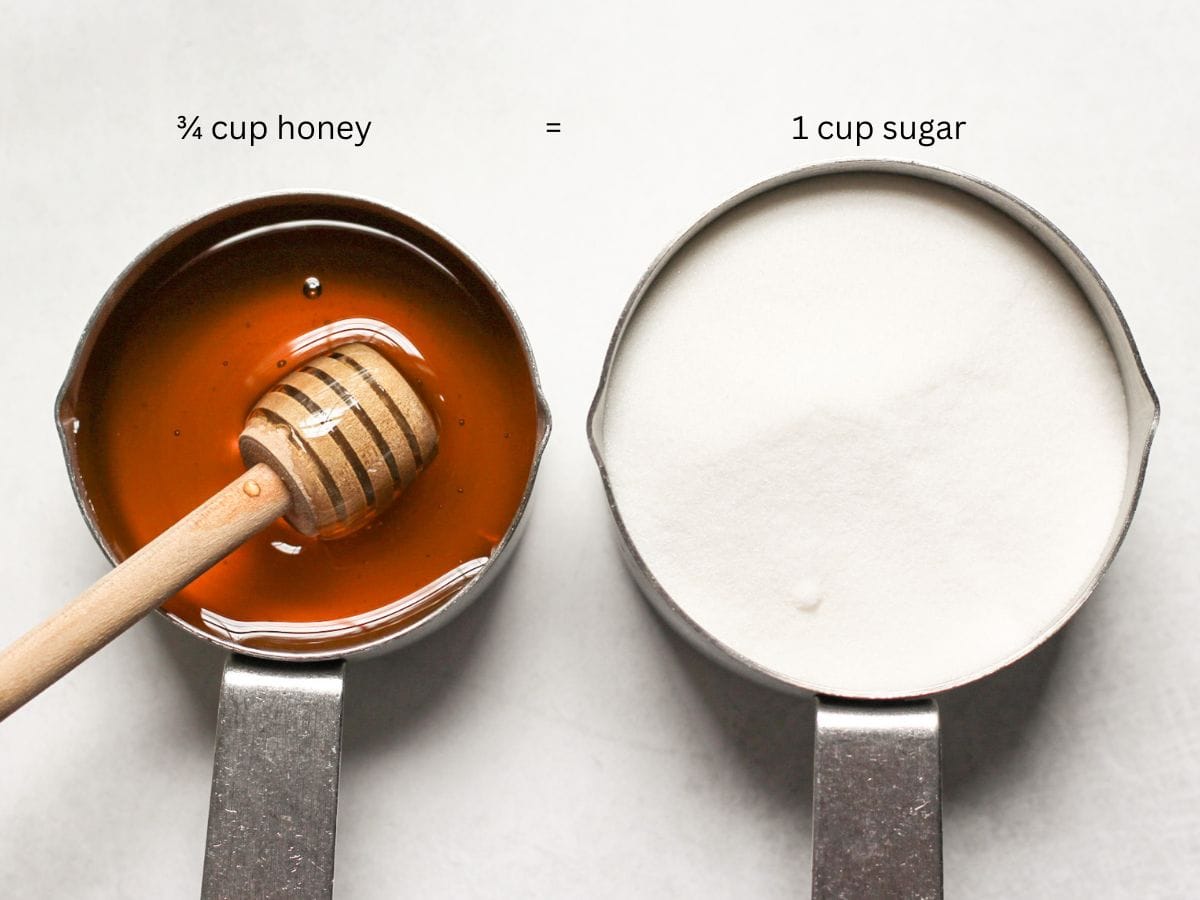 Overhead view of two stainless steel cups showing the 3:4 substitution ratio: one filled with 1 cup of sugar, and smaller one filled with ¾ cup of honey, 