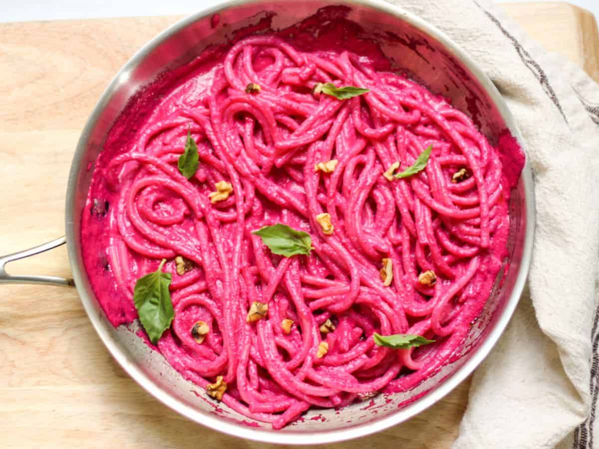 Spaghetti noodles tossed in a red beetroot creamy pasta sauce in a skillet. 